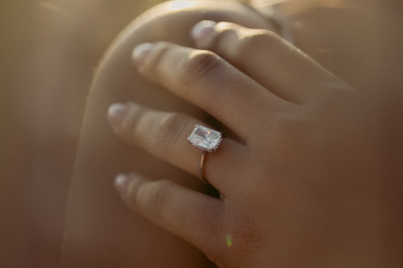 close up image of a woman’s hand resting on her should, adorned with a solitaire engagement ring