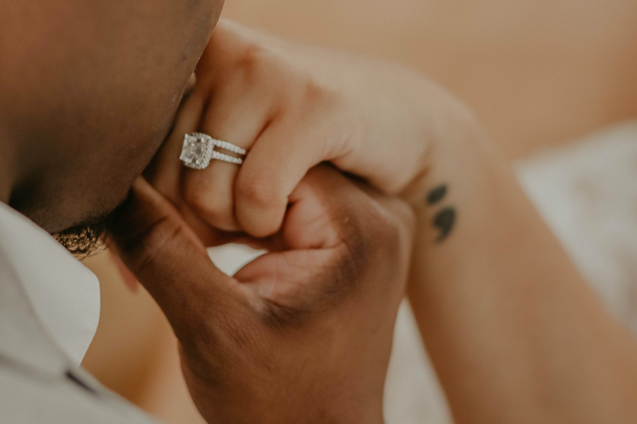 a man kissing a woman’s hand who is wearing a large, maximalist engagement ring
