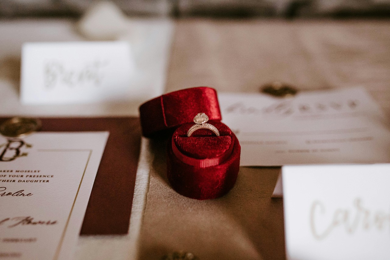 a red ring box on a lavishly set table holding a gold diamond engagement ring