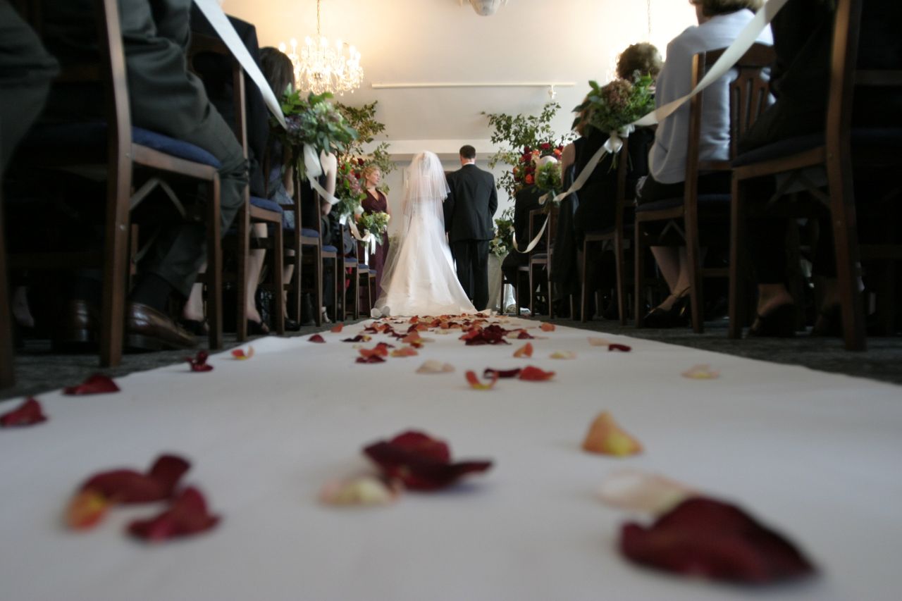 Rose petals dotting the aisle at a wedding with the bride and groom standing at the altar