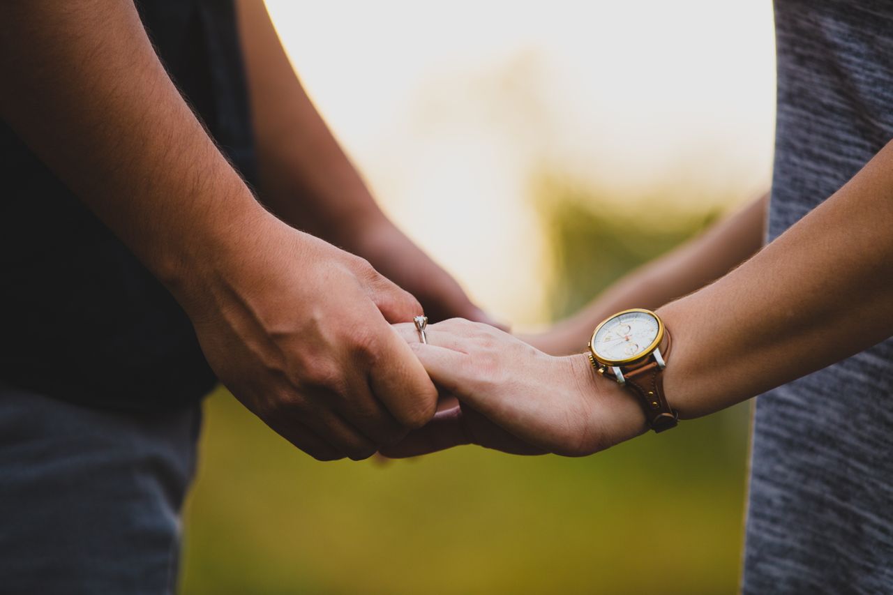 A couple holding hands with a solitaire engagement ring and watch in view