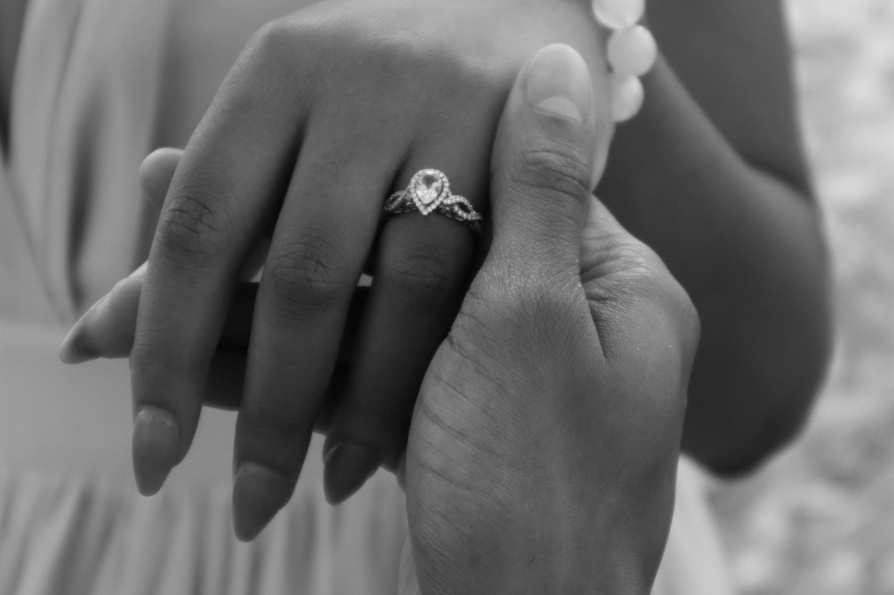 A woman wearing a pear shaped halo ring with an interweaving band is having their hand held by their love