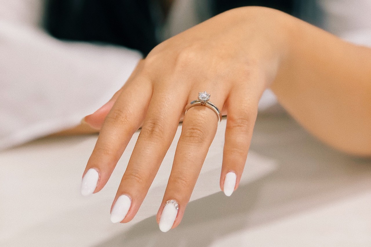 A woman with white almond shaped nails wearing a solitaire engagement ring