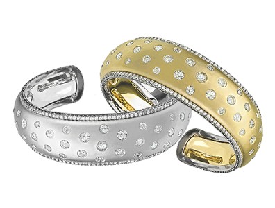 A white gold and a yellow gold cuff bracelets with diamonds lining the sides and dotted across the two bracelets by Jack Kelege