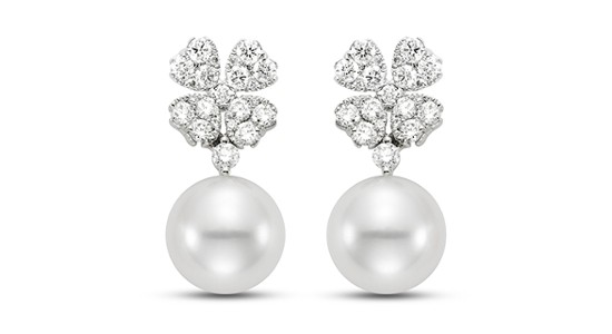 Close-up of two drop earrings featuring diamond studded clover motifs and pearls