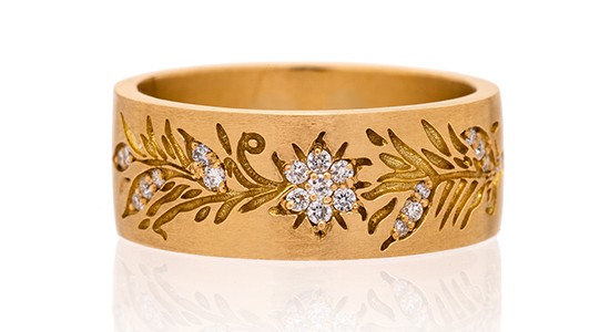 A thick gold bangle with engraved vines and diamond accents