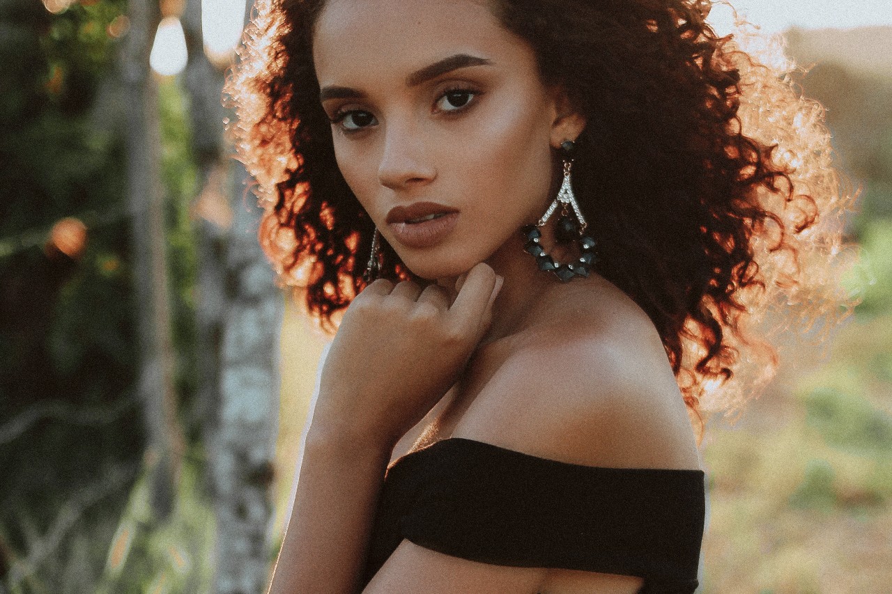 A model poses with emerald gemstone and diamond drop earrings in a field as the spring sun sets