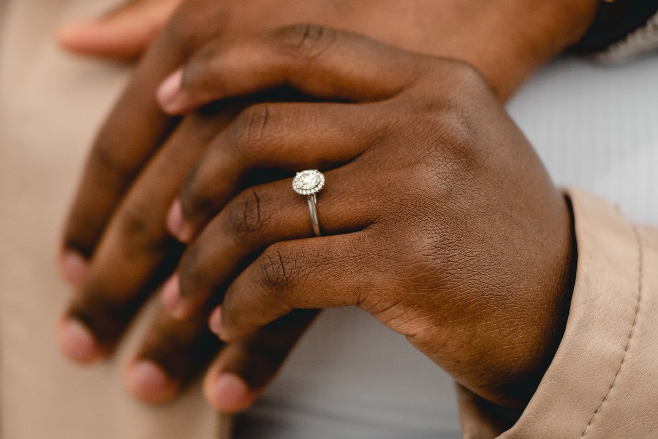Close up of two hands holding each other, the hand in the foreground donning an oval engagement ring