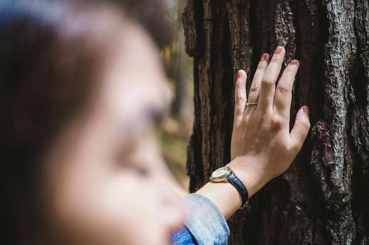 A woman props herself against a tree during a hike to show off her engagement ring