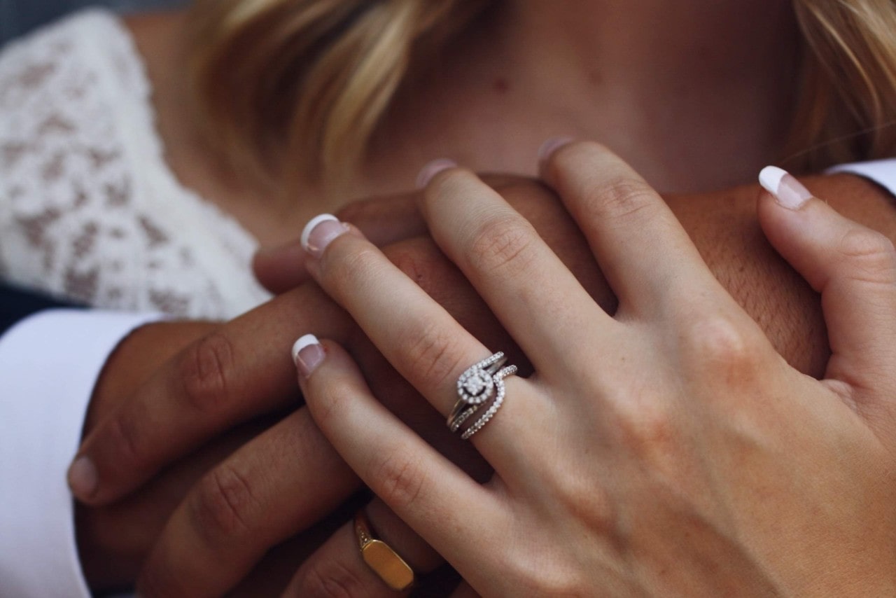 A bride places her hand over her grooms’ to show off her diamond bridal stack