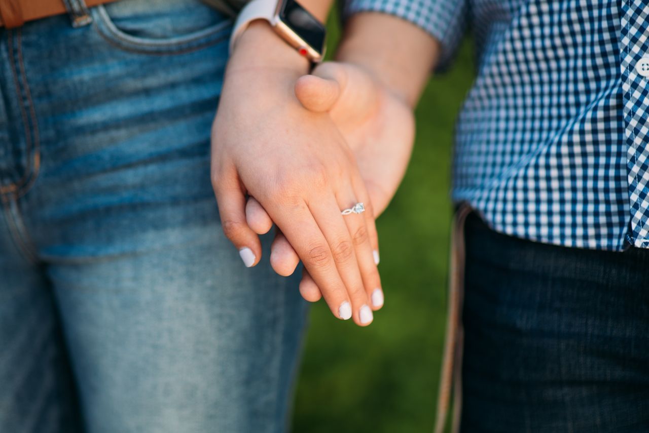 A woman holds hands with her lover and shows off her moissanite engagement ring