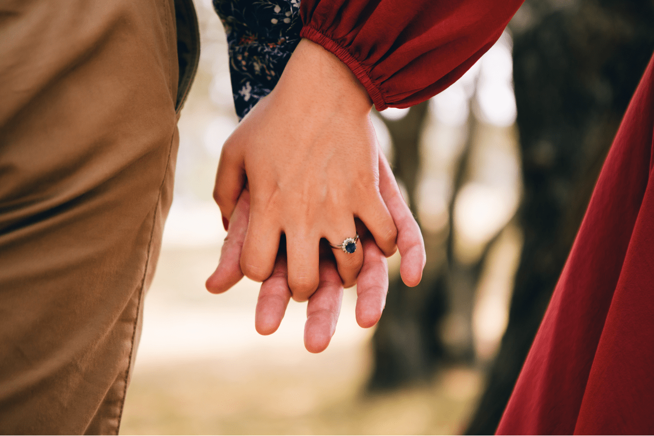 A woman holds her lover’s hand and shows off her sapphire halo ring