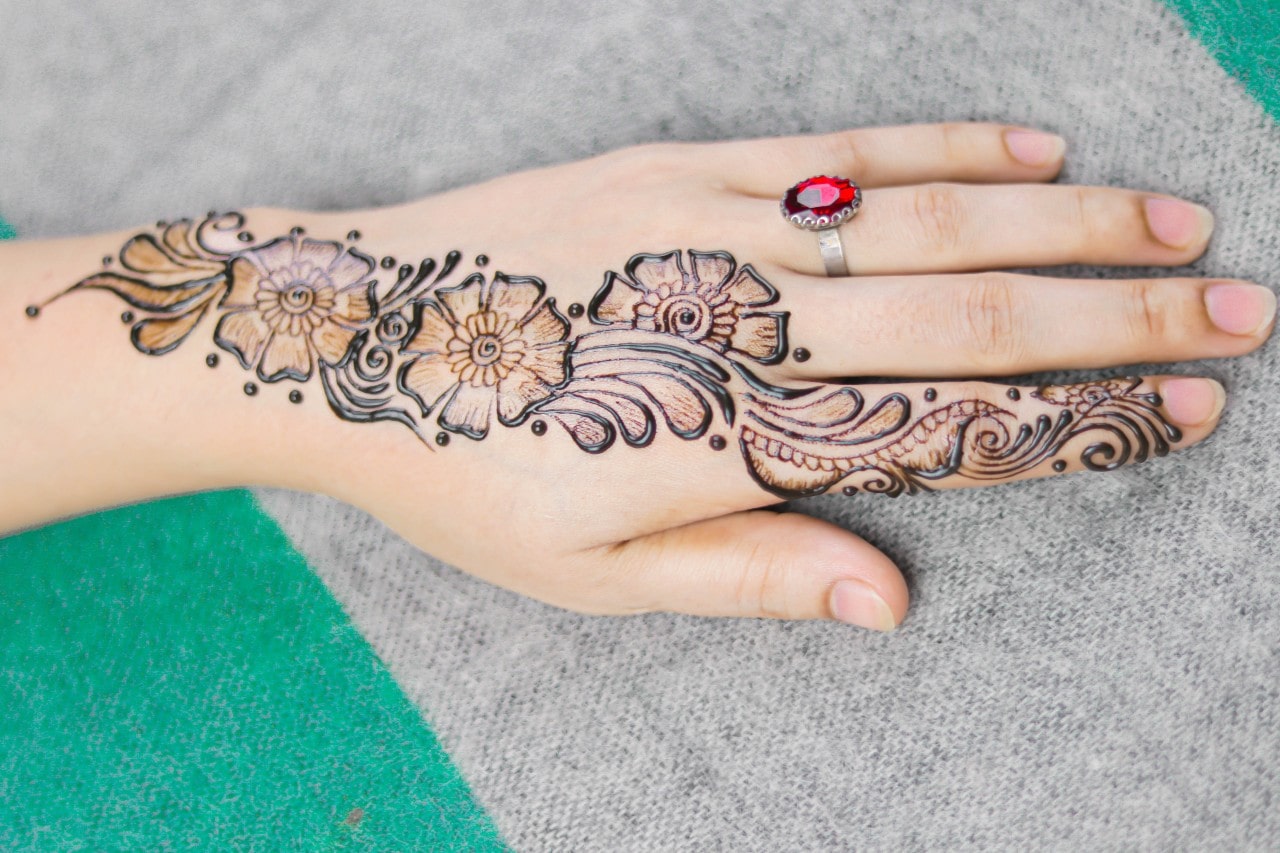 A woman rests her hand on a picnic blanket to show off her vintage-inspired ruby engagement ring while her henna dries