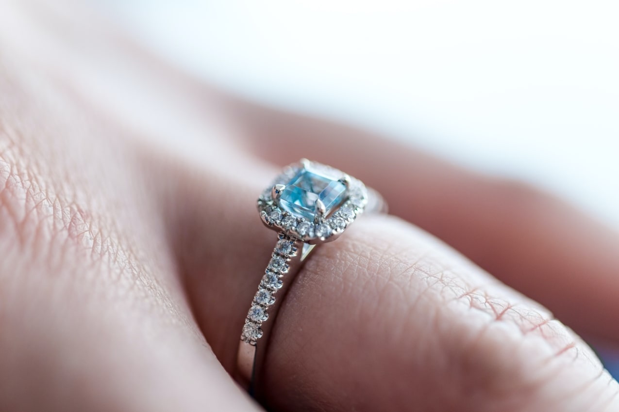 A woman wearing a yellow gold halo engagement ring with a cushion-cut blue topaz stone