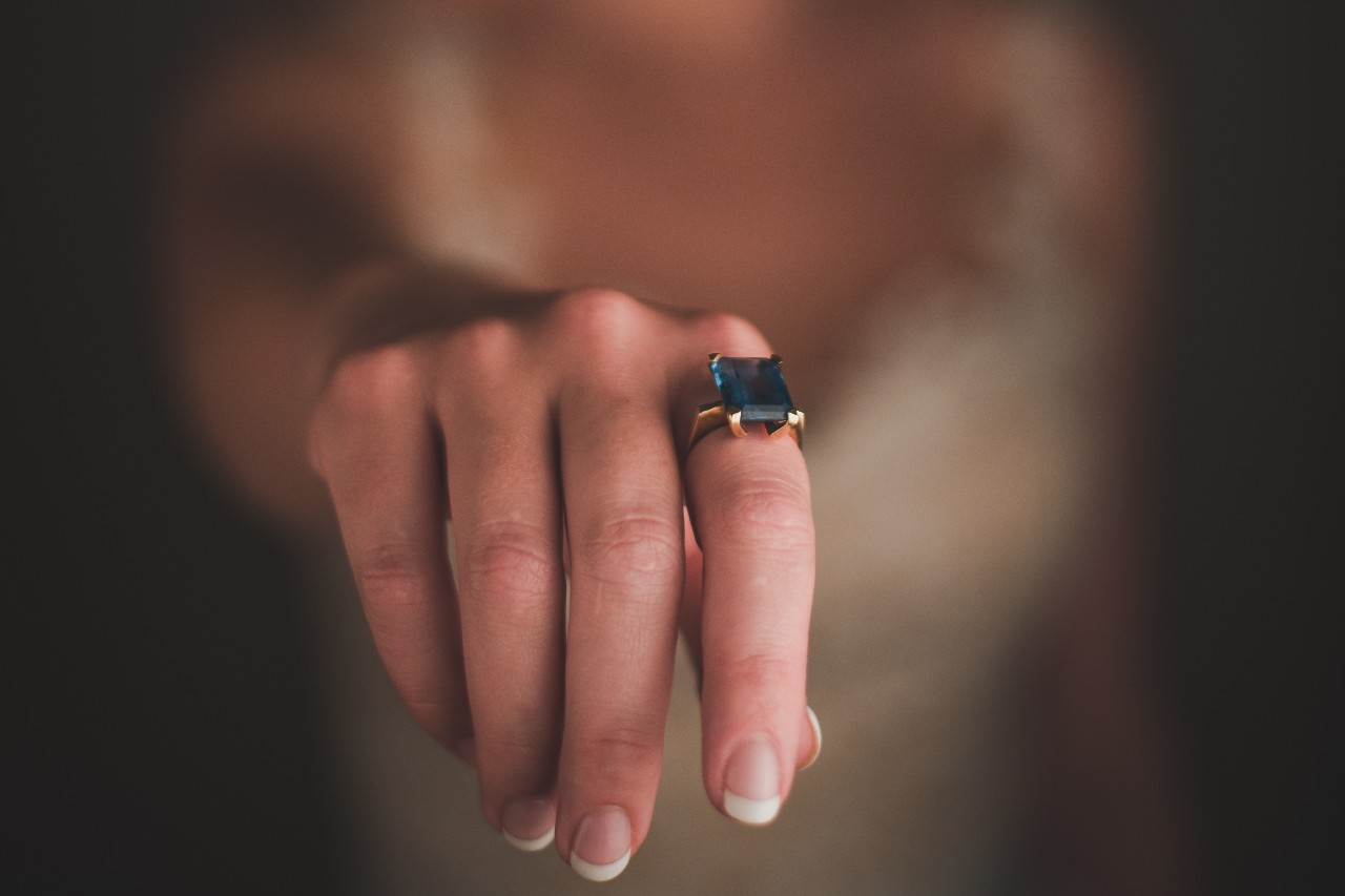 A bride stretches her hand out to show off her emerald-cut sapphire solitaire engagement ring