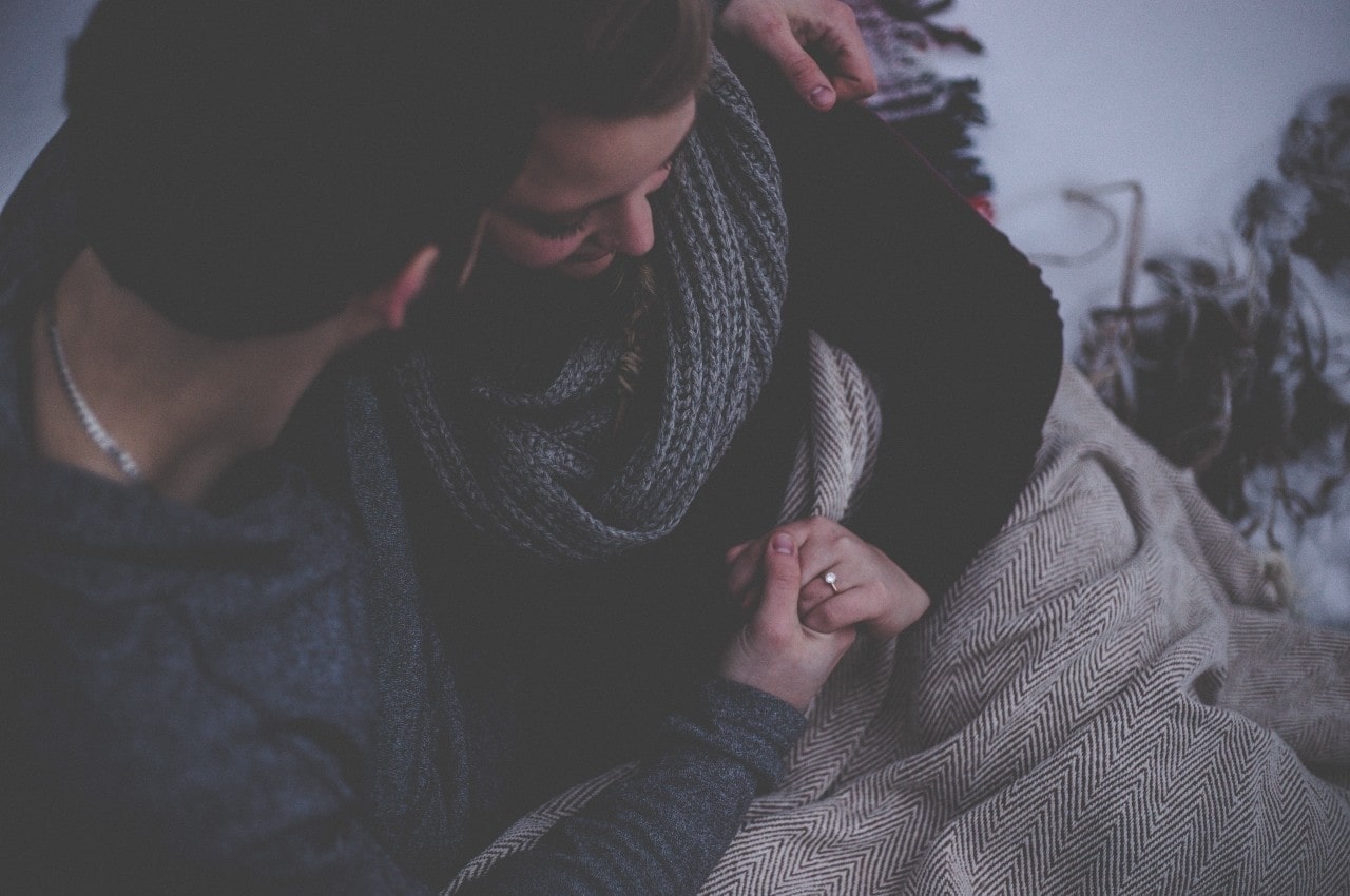 A happy fiancee admires her engagement ring while snuggled up with her partner