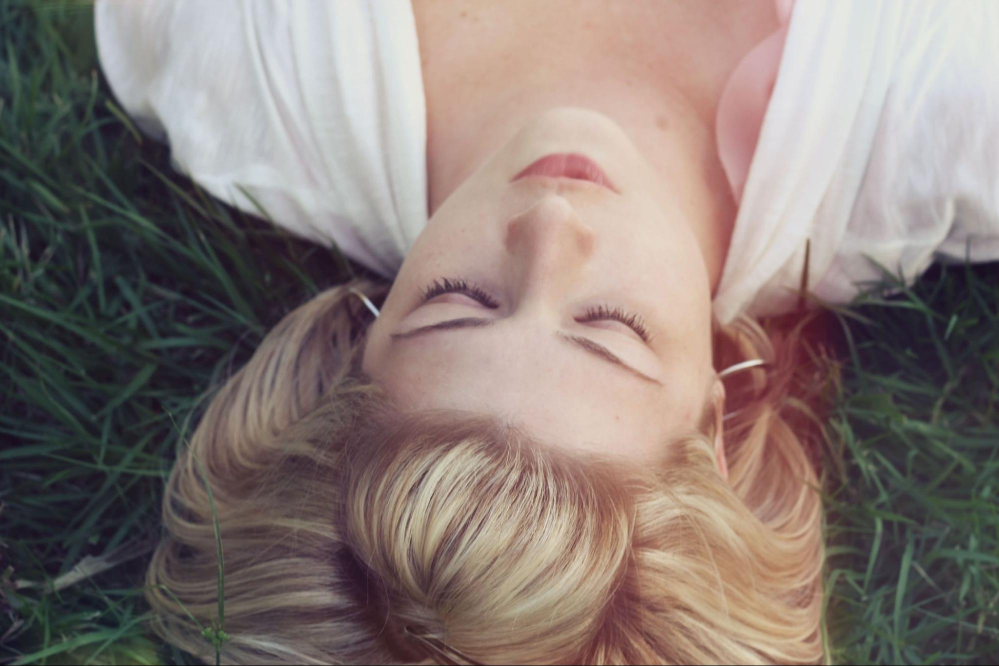 A woman wearing silver hoop earrings and a white top lies in the grass