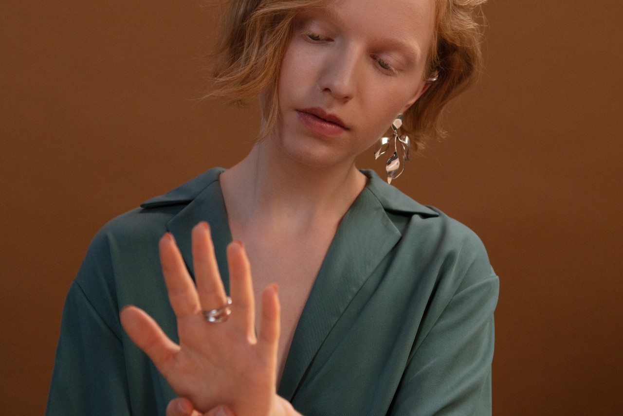 A woman in a green dress shirt admires her silver jewelry