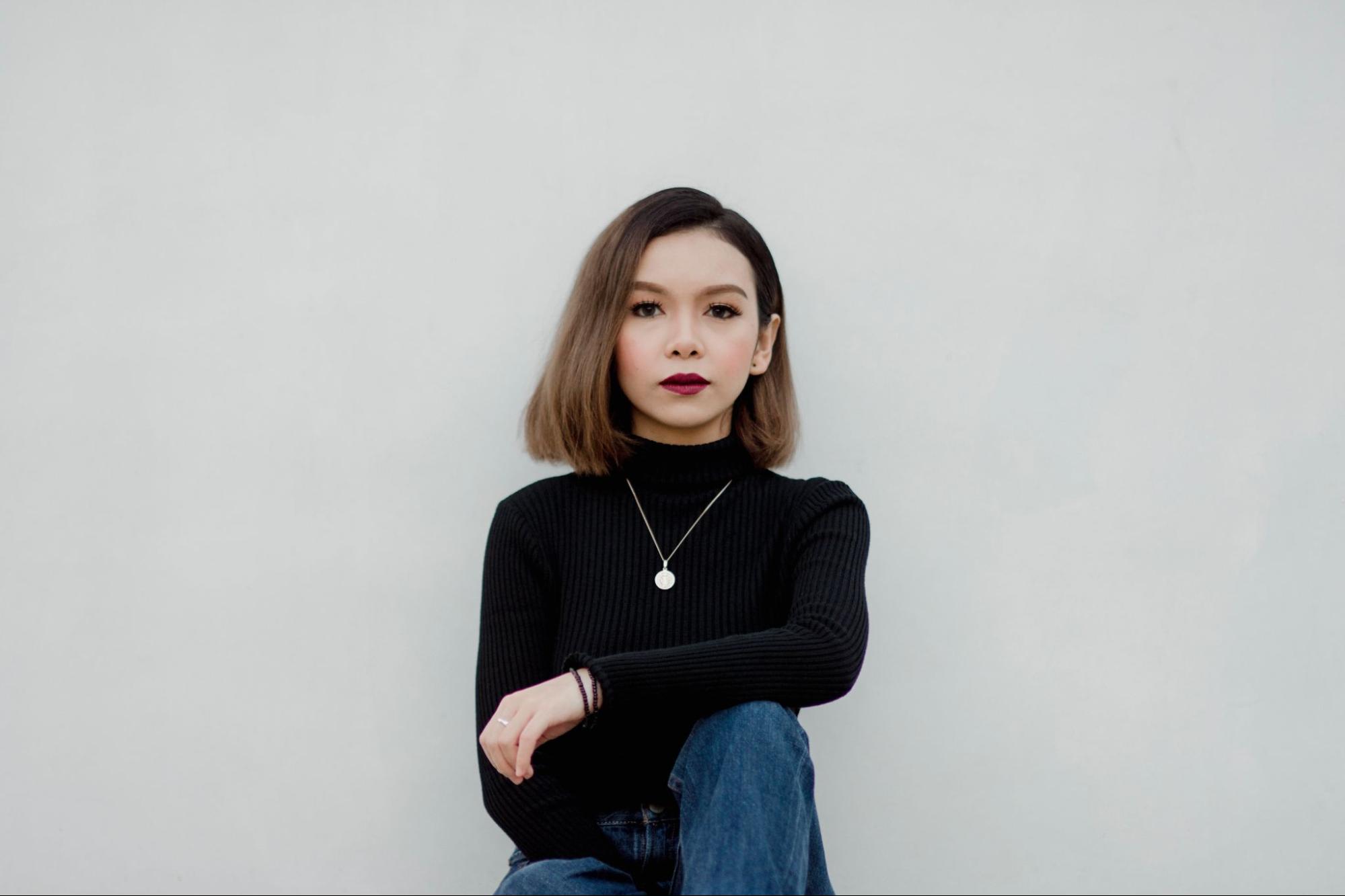 A woman in a black sweater and red lipstick wearing a gold medallion necklace