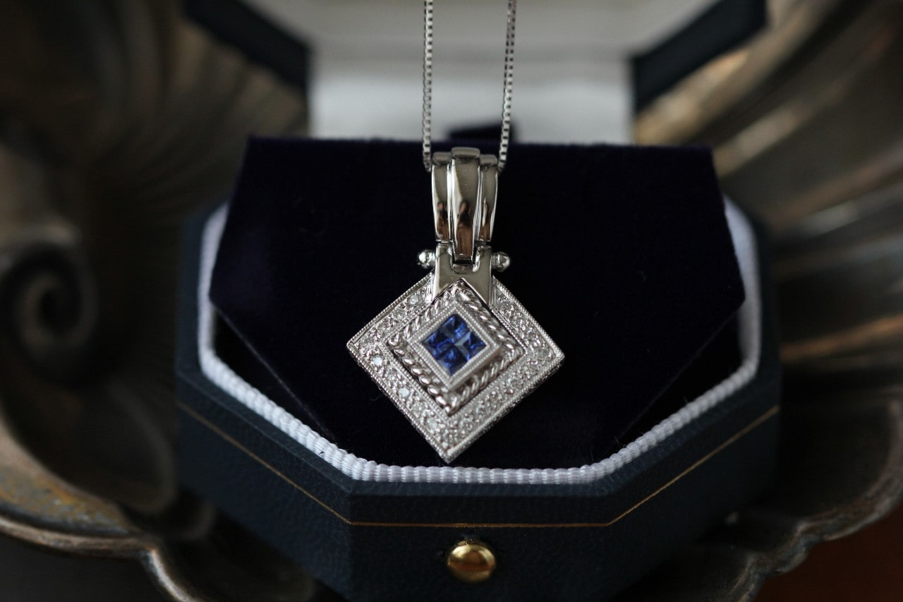 a white gold necklace in a box with a sapphire center stone
