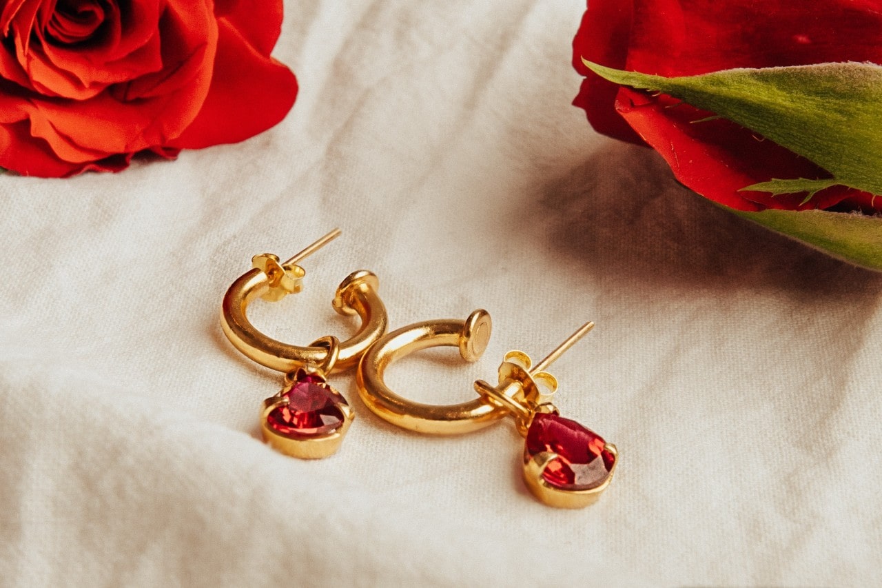 a pair of yellow gold huggie earrings featuring pear shape rubies