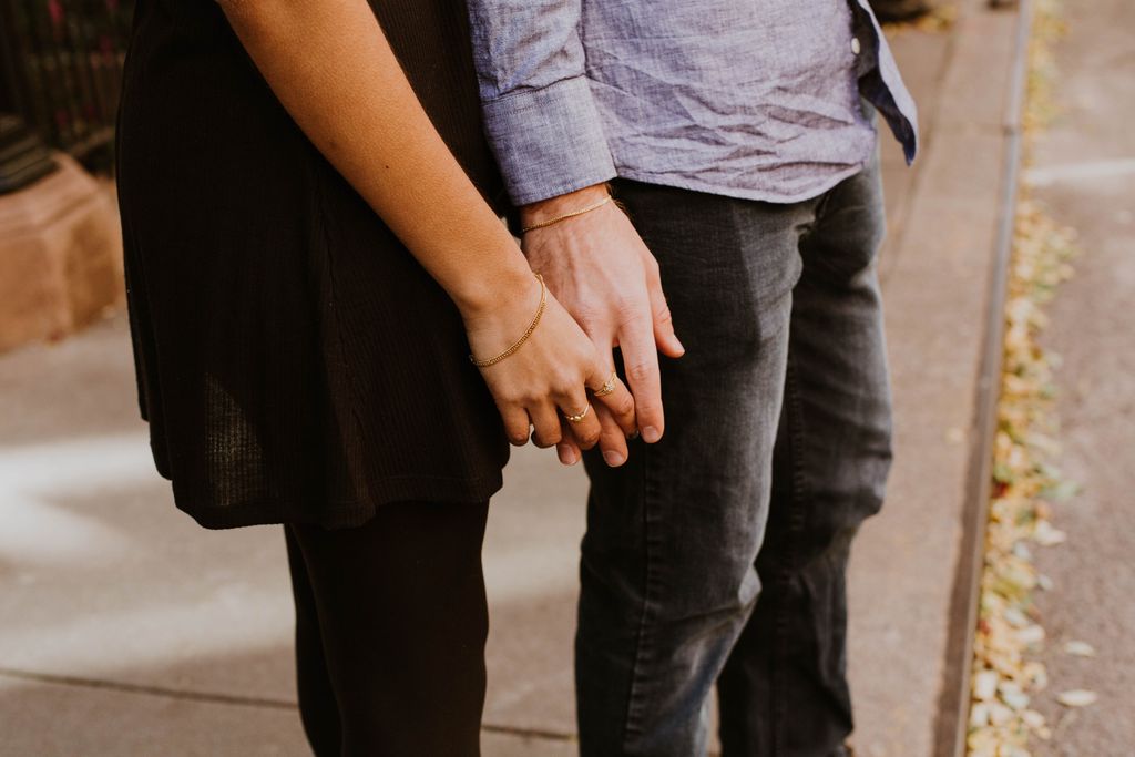 A close-up of a couple holding hands, each wearing delicate jewelry.