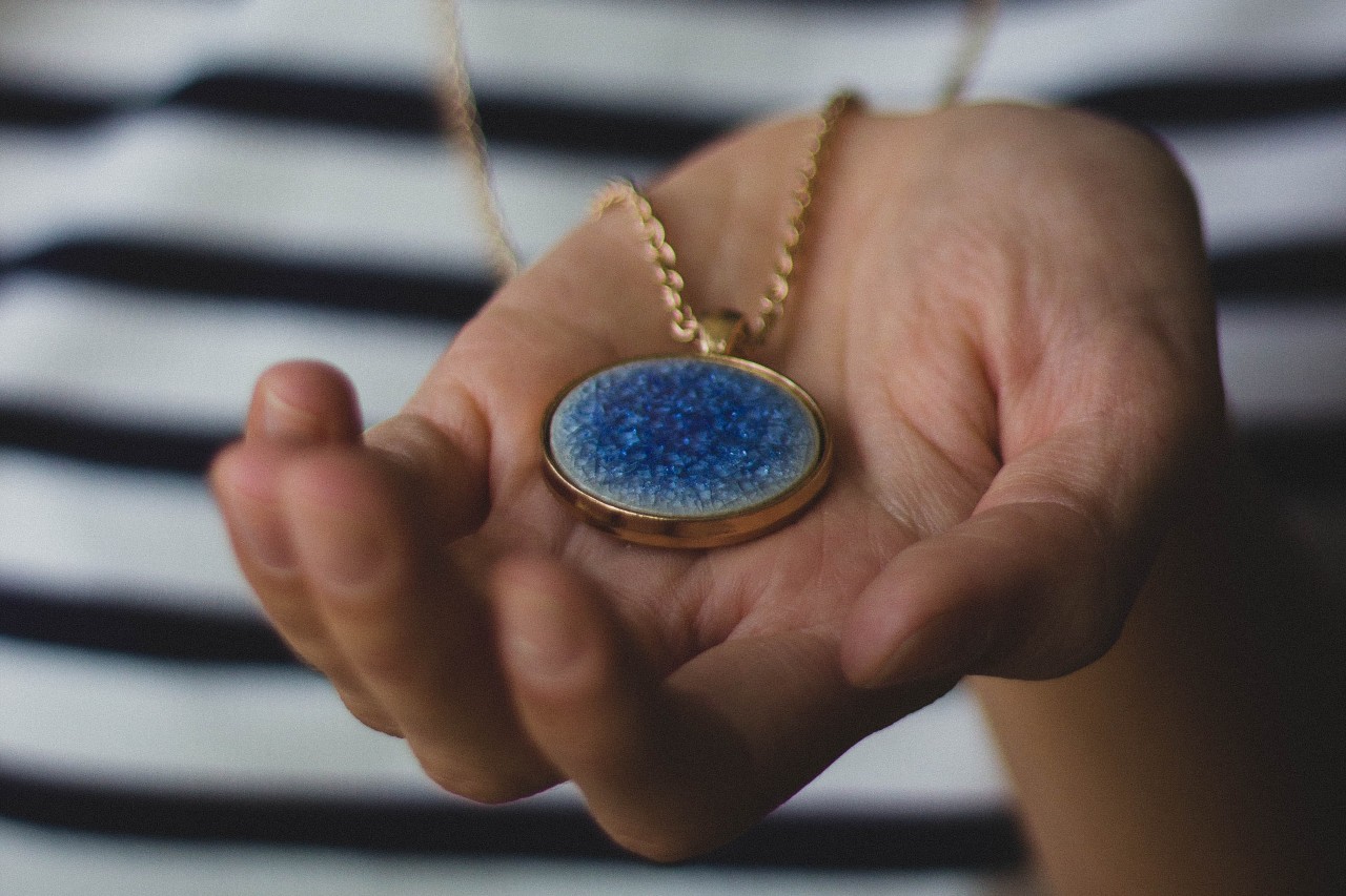 A close-up of a person holding a gold necklace with a bezel set stone pendant in the palm of their hand.