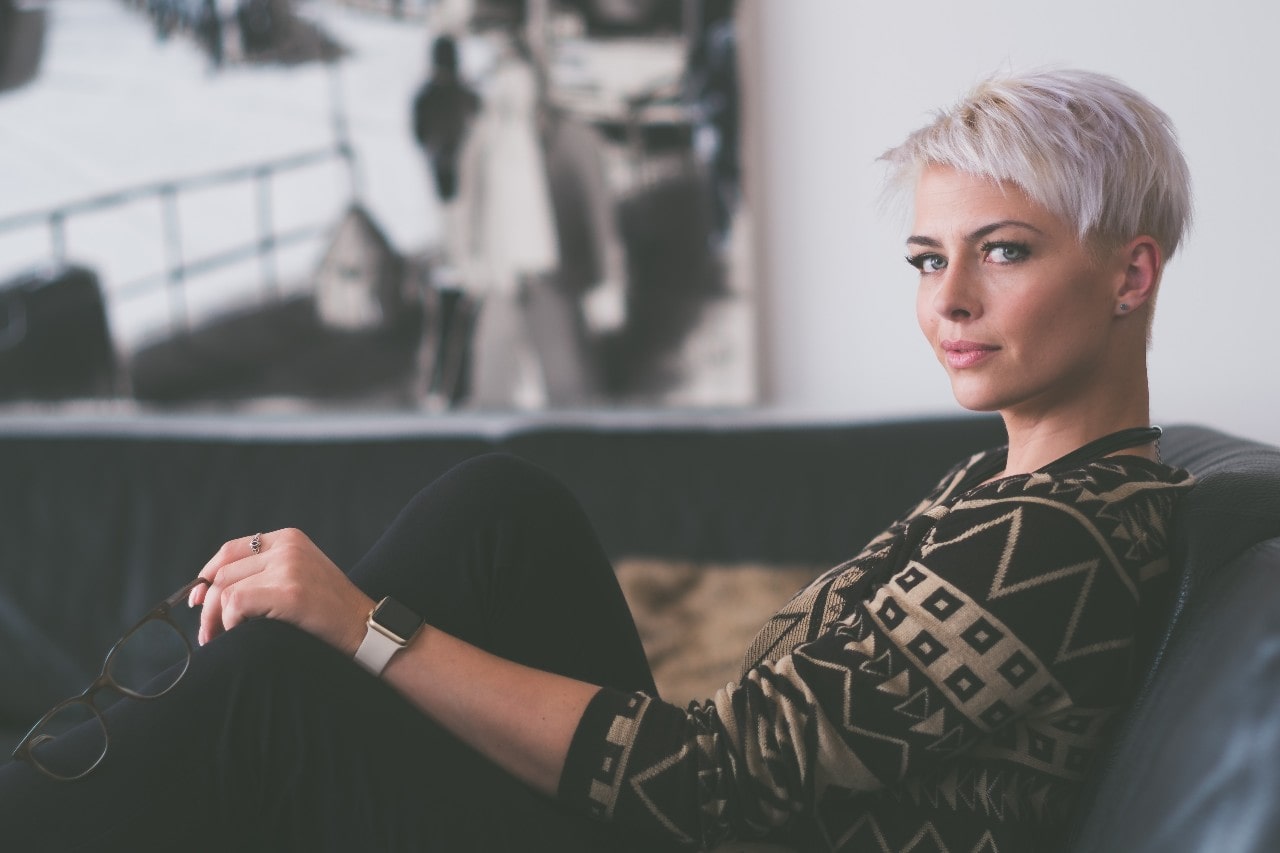 A fashionable woman lounging on a leather sofa, wearing stud earrings and a smartwatch.