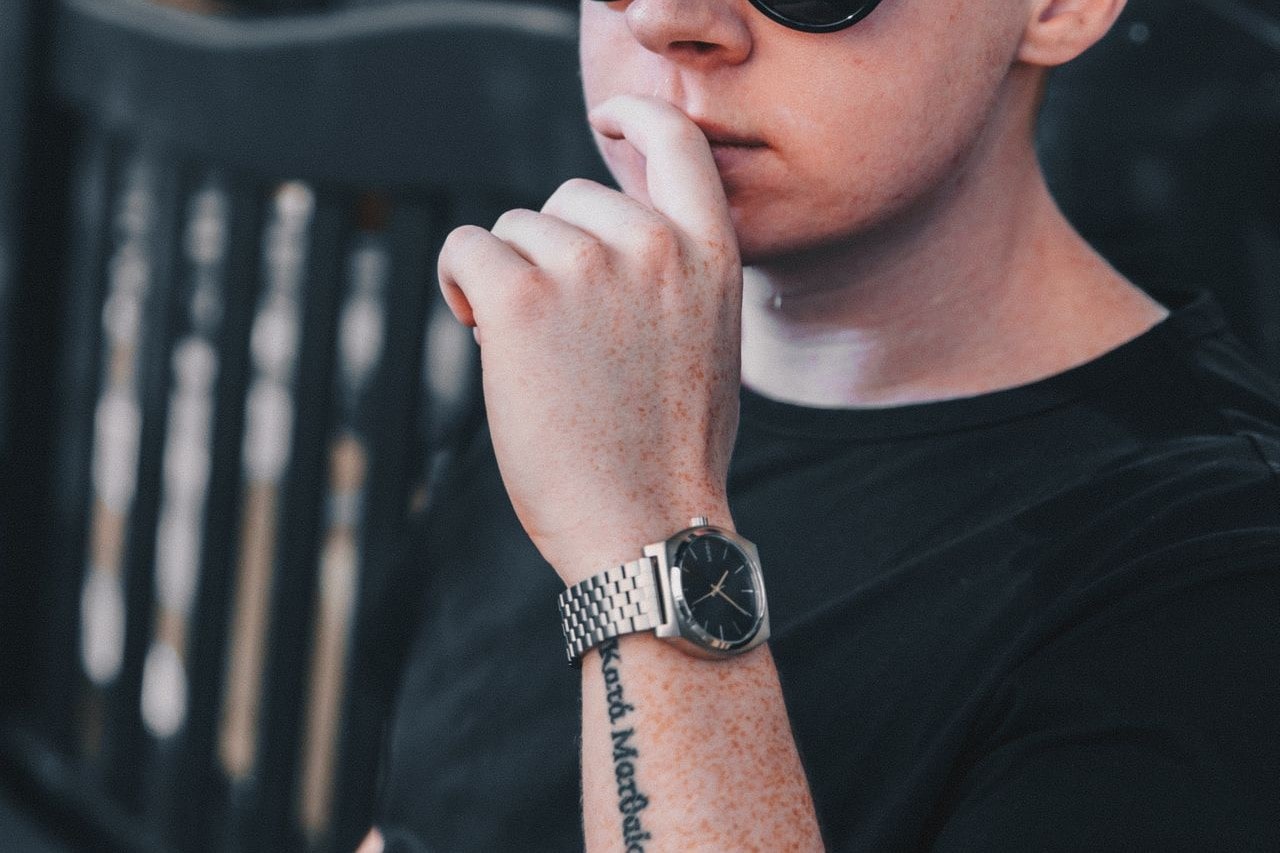 a casual man wearing a sterling silver watch sits on a park bench.