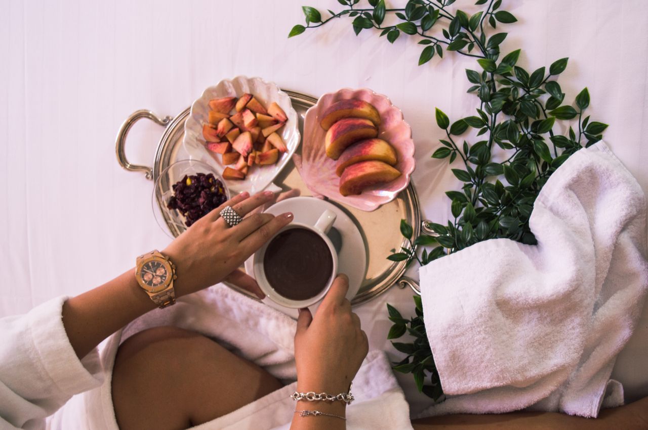 A woman lounges in a robe with cut fruit and coffee with a gold watch and jewelry.