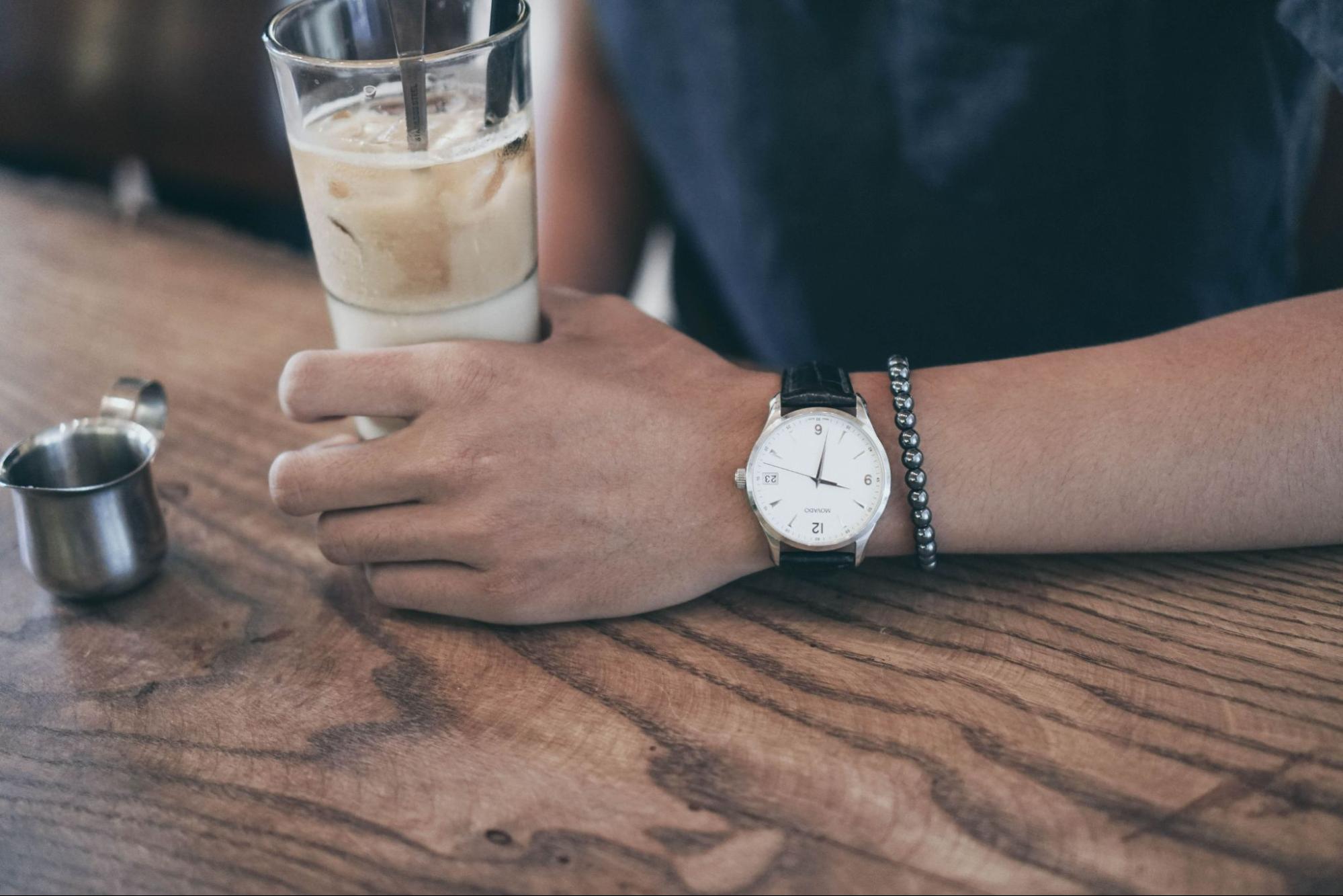 A man sipping an iced coffee wears a casual watch.