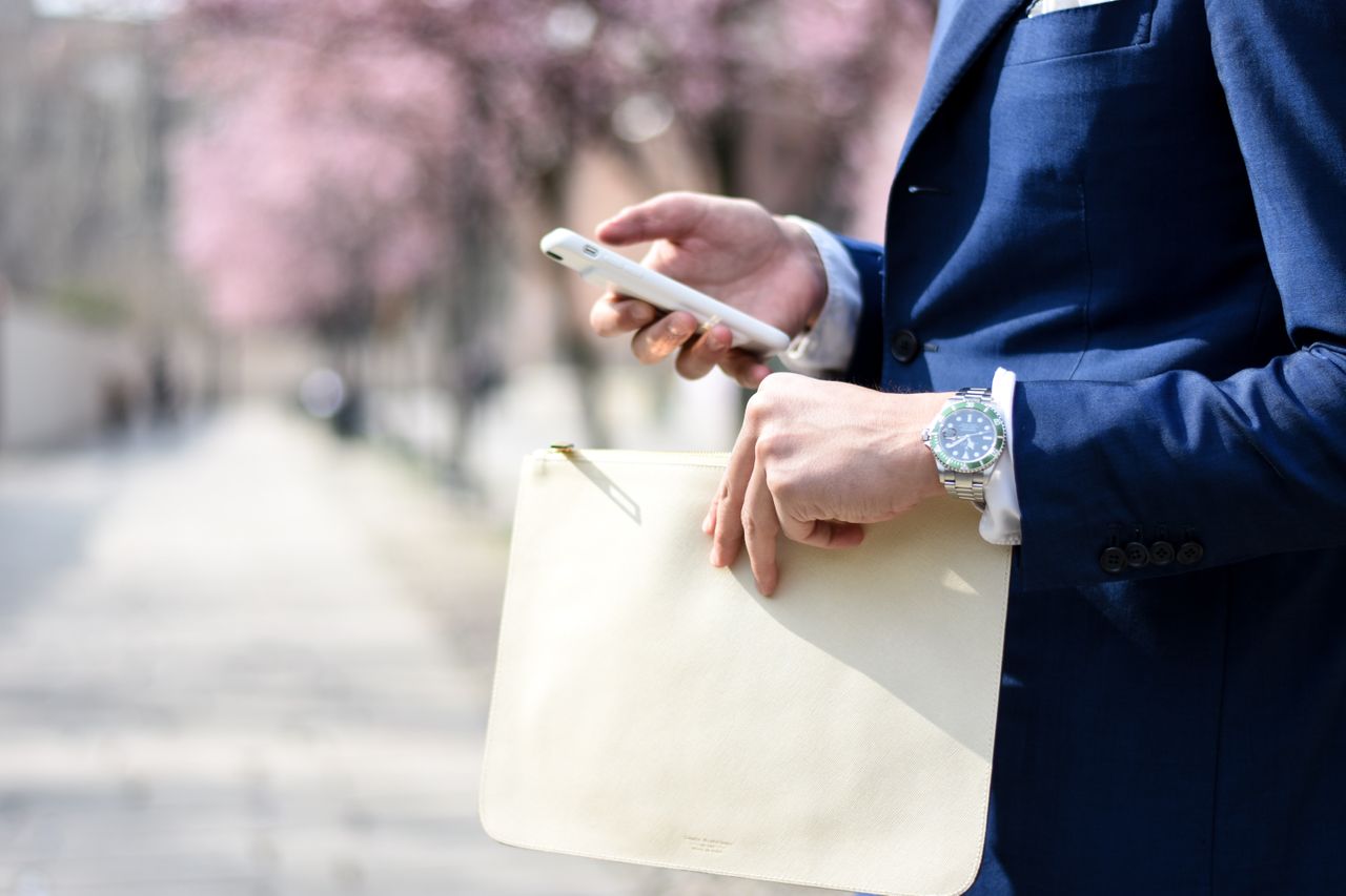 A business man holds a folder while texting on a walk outside.