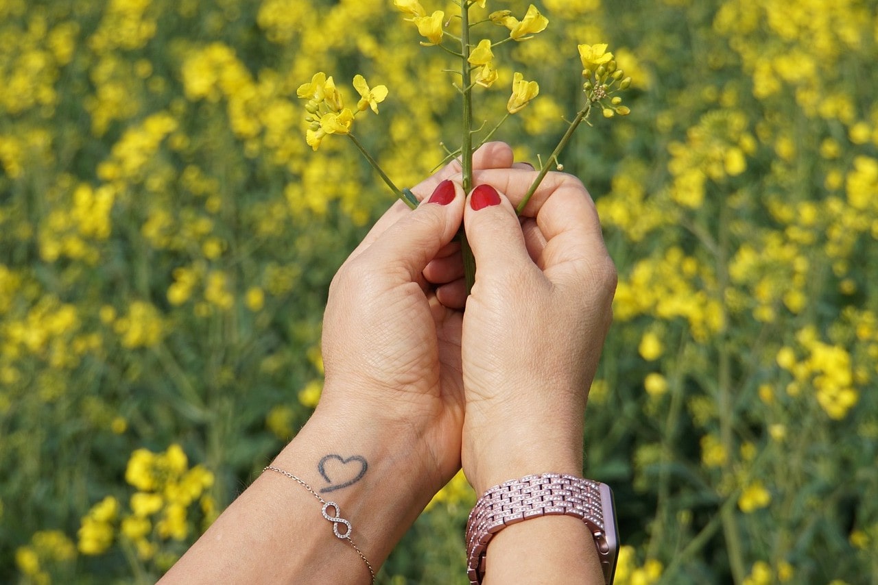 A woman’s hands, adorned in a delicate bracelet and a diamond-accented watch, holding yellow flowers.