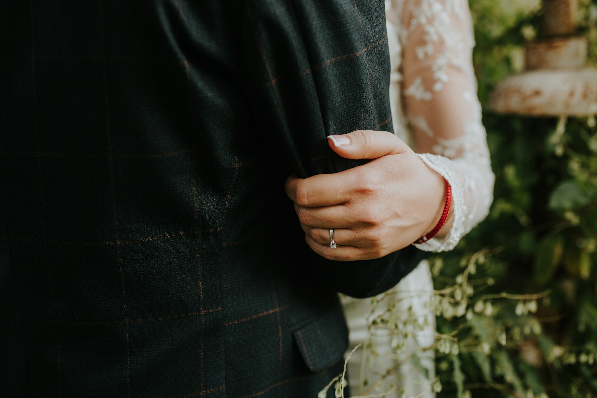 A bride places her hand on groom’s arm in a checkered suit, showcasing white gold solitaire wedding band