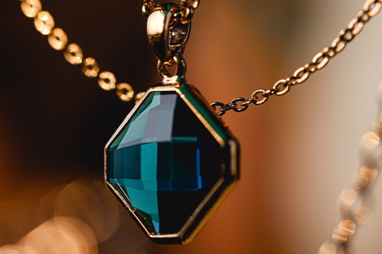 a bold pendant necklace featuring a deep blue green gemstone and a gold chain