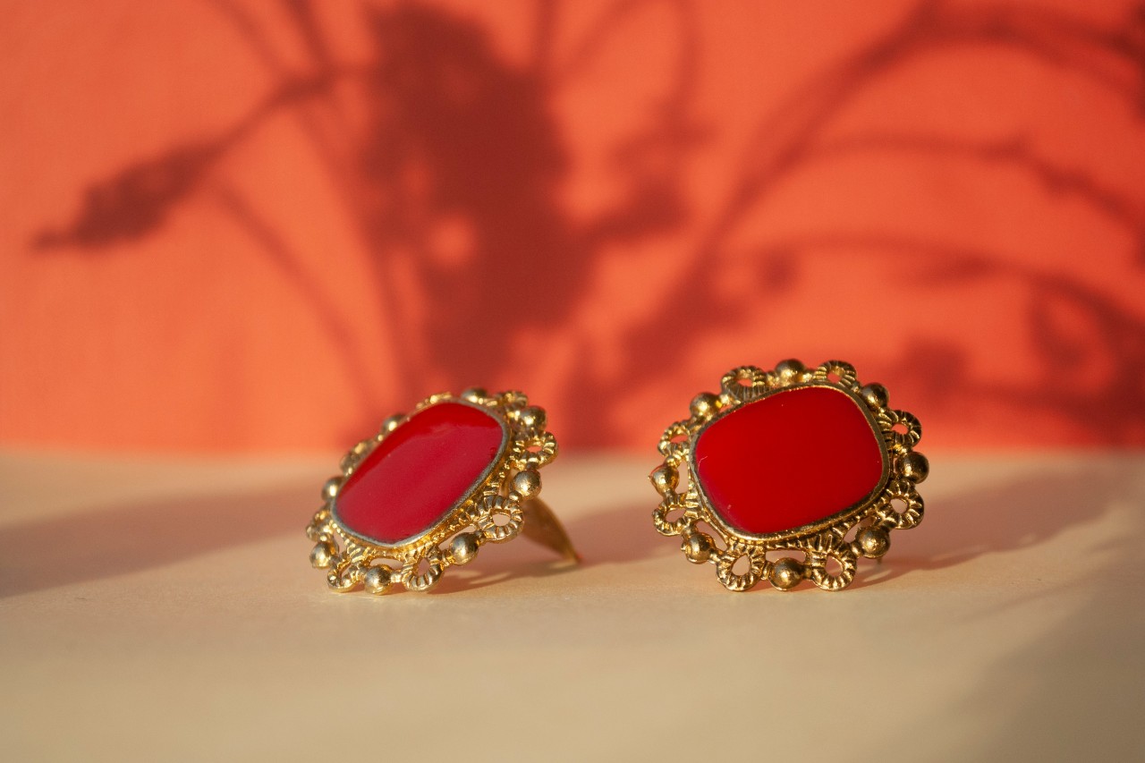 a pair of yellow gold stud earrings with red centers on a beige surface