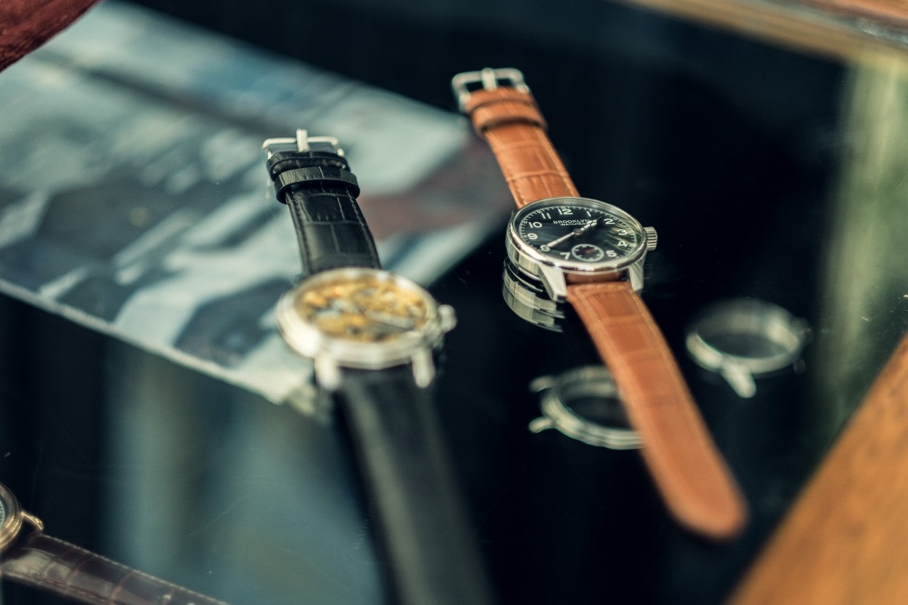 Three wristwatches resting on a tabletop, the third out of focus on the side.