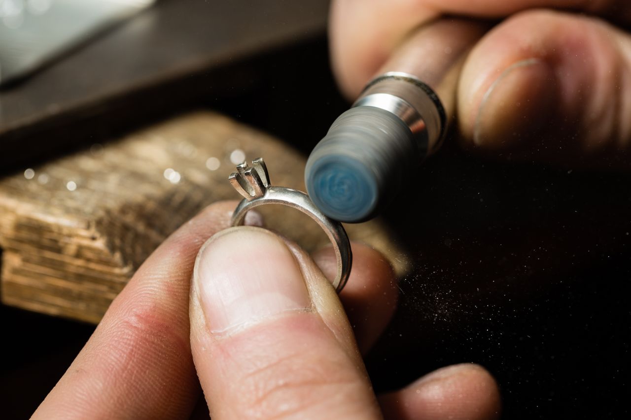 A jeweler polishes a silver ring setting using a rotary tool.