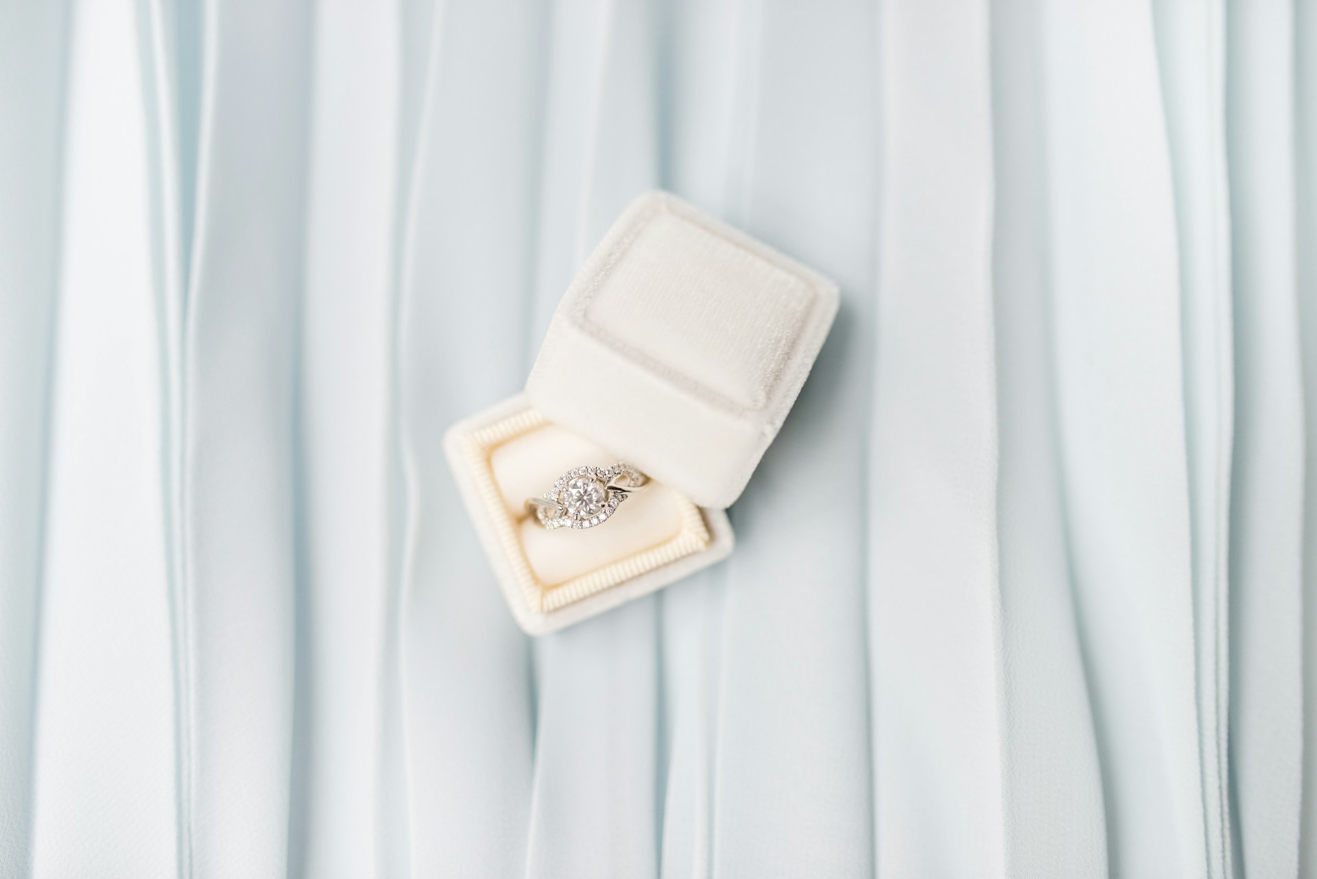 a halo engagement ring in a white ring box on a piece of folded blue fabric