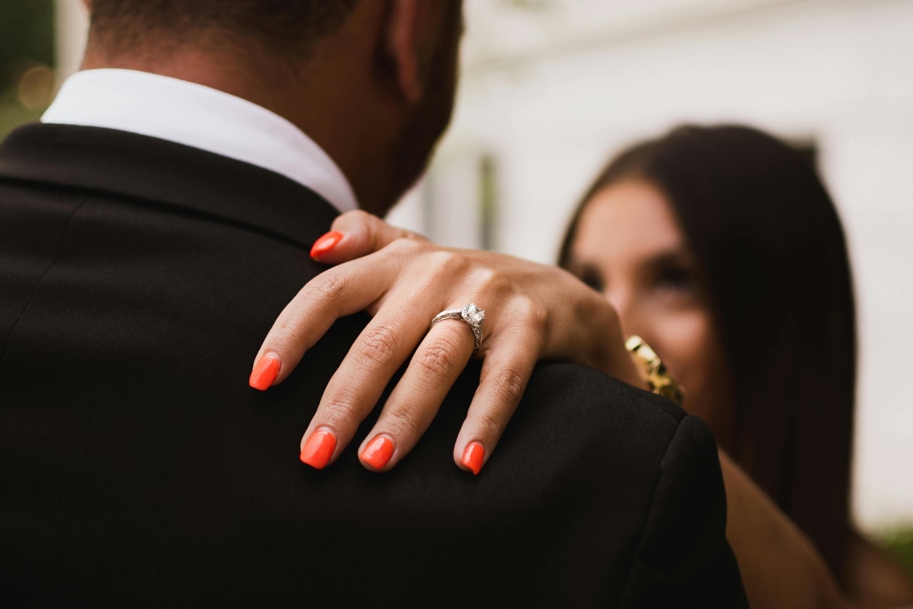 a woman resting her hand on a man’s shoulder with a wide band engagement ring