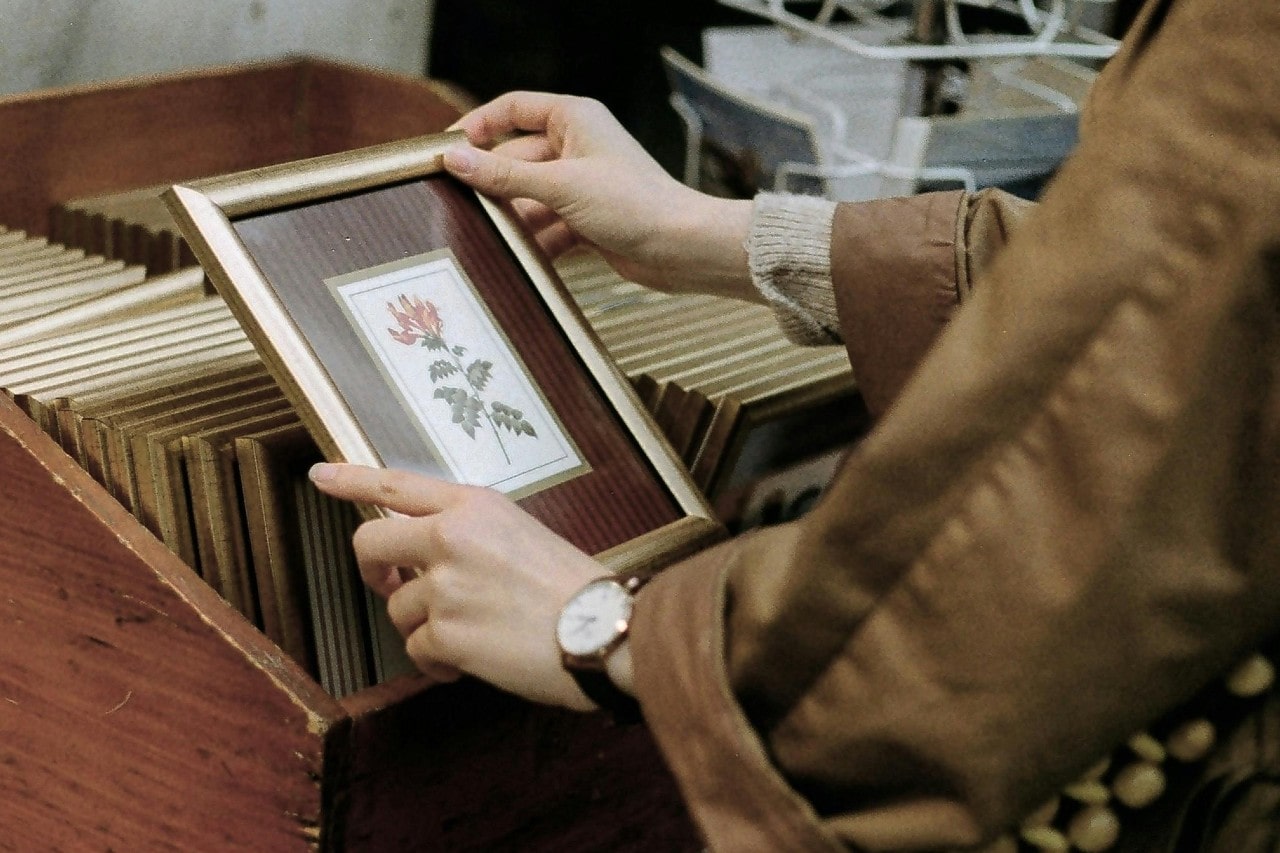 A person looking through vintage picture frames and wearing a white and gold watch.