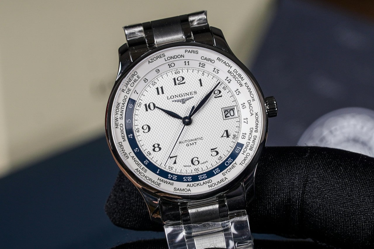 A close-up image of a Longines watch held by a black-gloved hand.