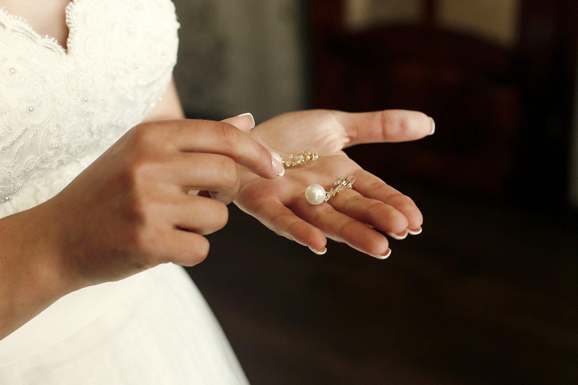 a woman’s hand holding two pearl earrings