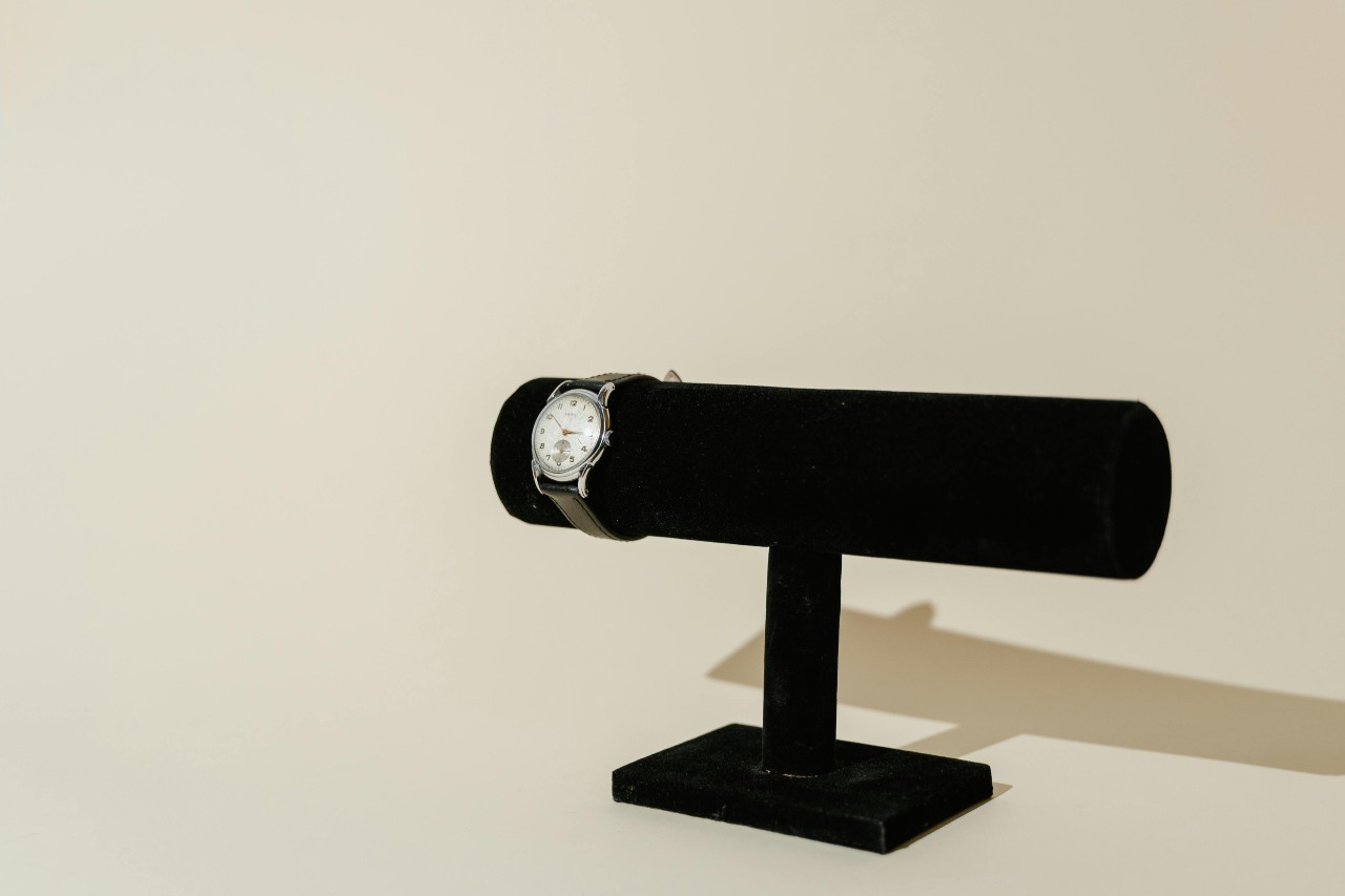 A wide view of a dress watch with a black leather strap displayed on a black velvet watch stand.