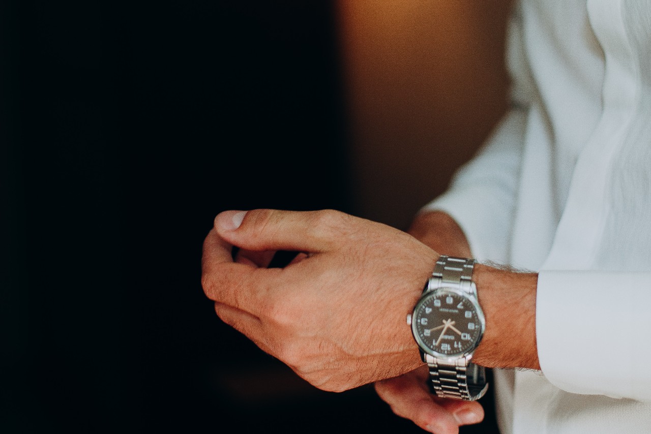 A close up of a man in the white shirt fixing his stainless steel black dial wristwatch. A close up of a man in the white shirt fixing his stainless steel black dial wristwatch.