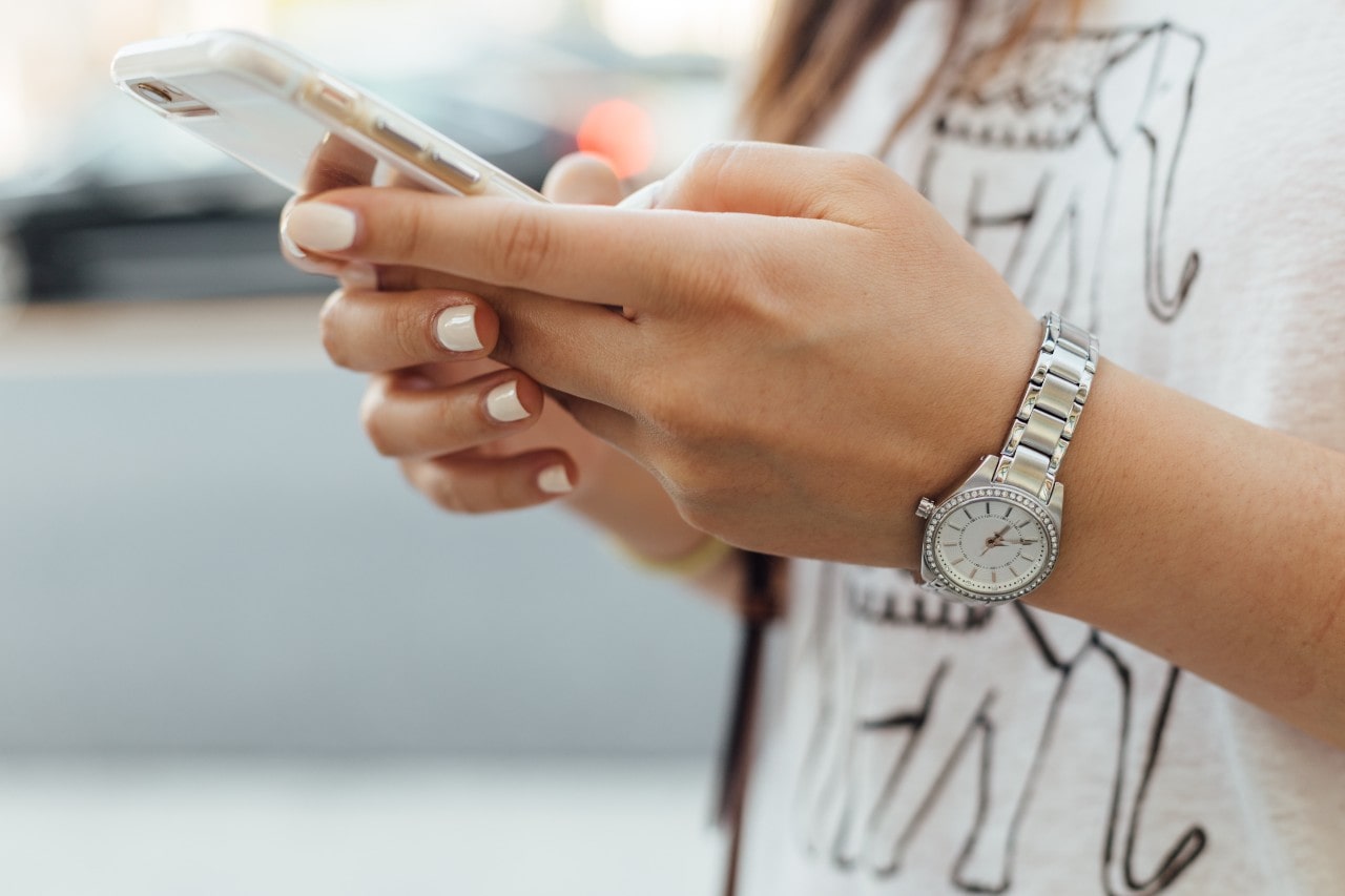 A close up of a woman with white manicure and printed t-shirt typing on a phone, showcasing stainless steel wristwatch. A close up of a woman with white manicure and printed t-shirt typing on a phone, showcasing stainless steel wristwatch.