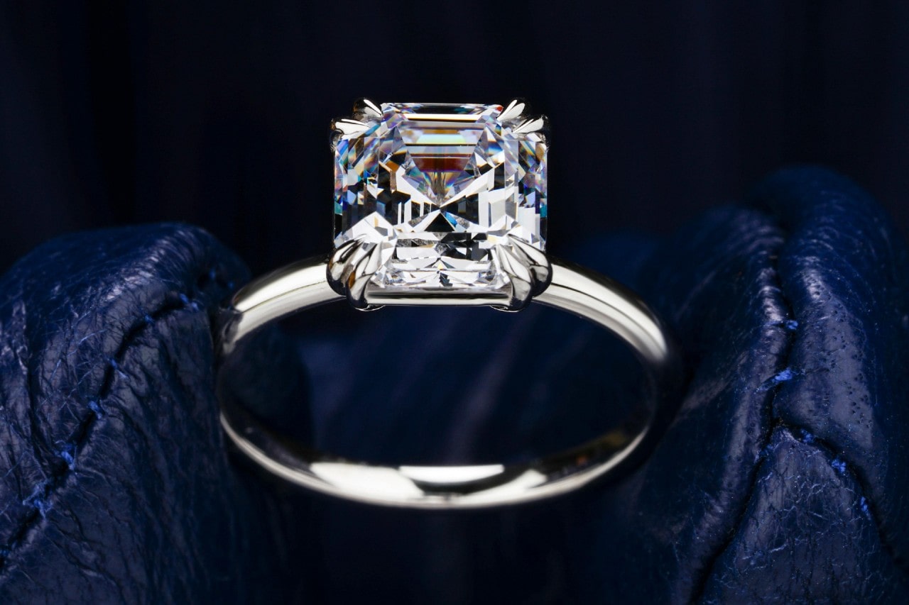 a white gold engagement ring with an asscher cut center stone held by gloved fingers