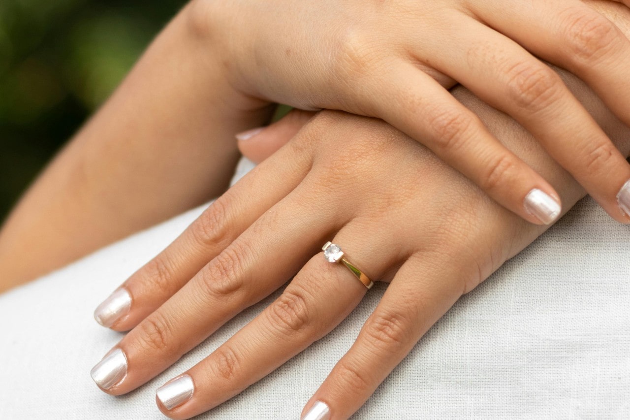 A woman’s hands on someone’s back, one of them adorned with a dainty engagement ring.