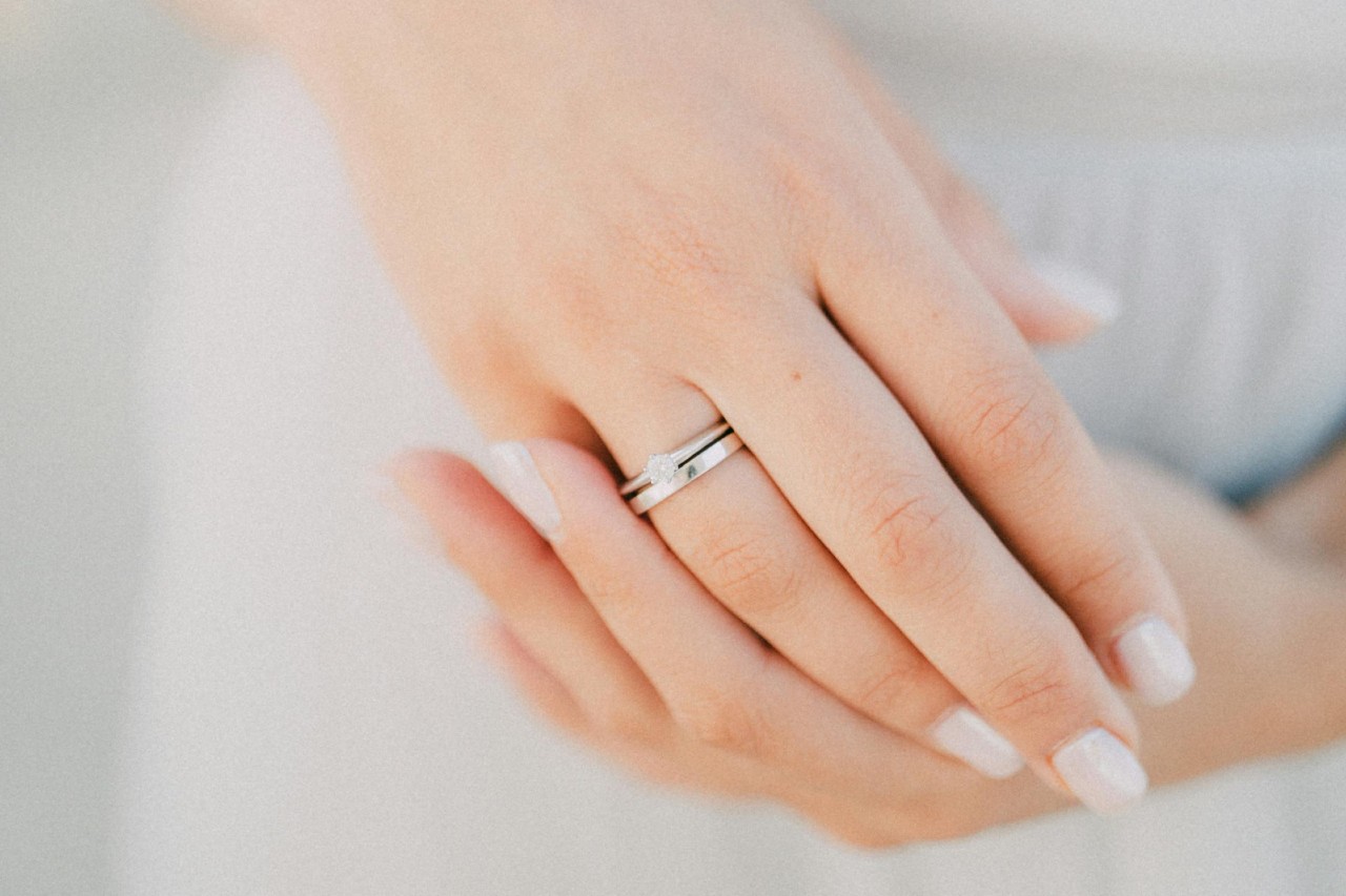 A bride’s hands, one of which is adorned with a white gold engagement ring and wedding band.