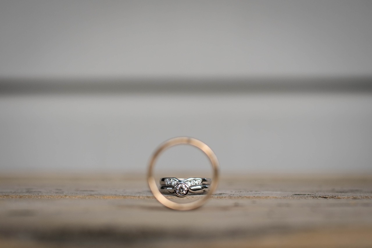 A diamond wedding band displayed through the focus of a gold ring, set on a wooden surface